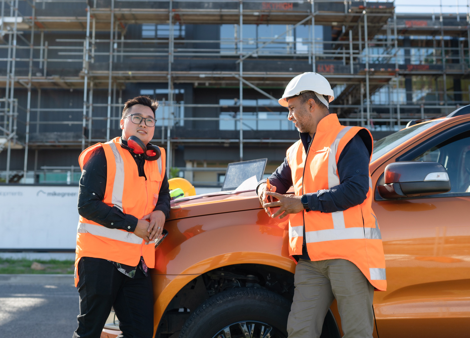 Two males in high vis vests talking on a building site.