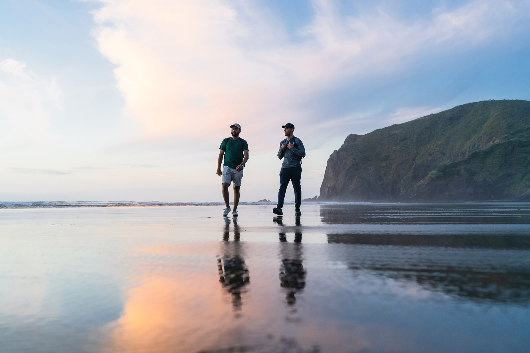 Two males in active wear walking along a kiwi beach at golden hour